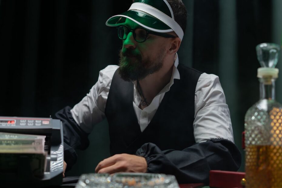 Bearded croupier in casino setting wearing visor and counting cash.