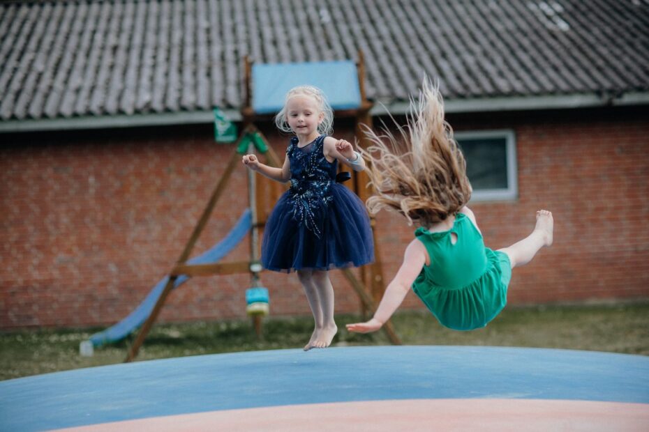 Two girls enjoy jumping on a trampoline outside. Fun and laughter in a playful setting.