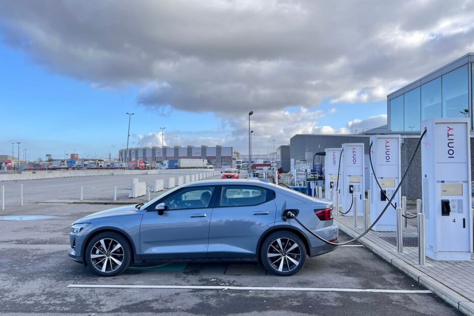 A sleek electric car charging at an Ionity station on a cloudy day in an industrial area.